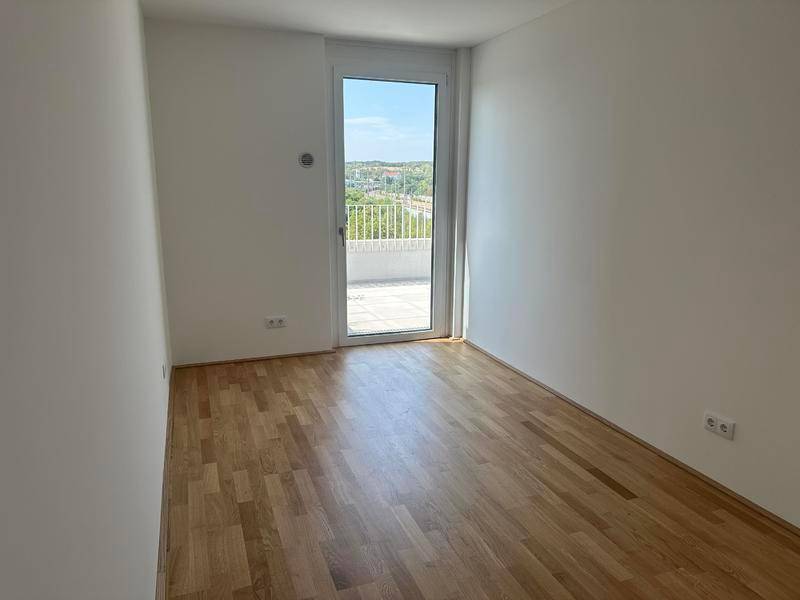 Schlafzimmer mit Holzboden und Zugang zu einem Balkon, bietet viel Tageslicht.