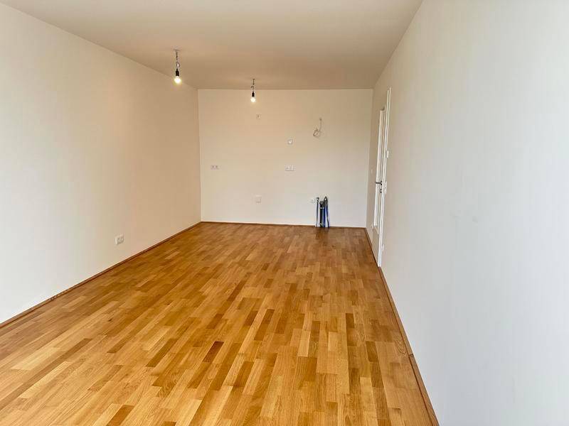 Leerer Raum mit Holzboden und Anschlüssen für eine zukünftige Küche.