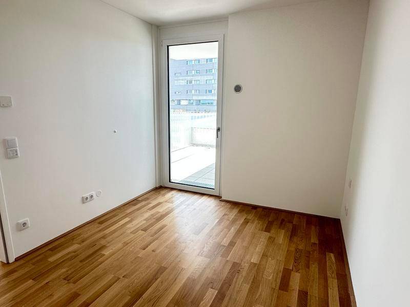 Helles Zimmer mit Parkettboden und Zugang zu einem Balkon oder einer Terrasse.
