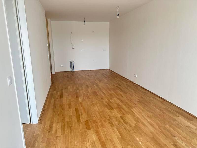 Leerer Küchenbereich mit Parkettboden und Anschlüssen für eine Einbauküche.