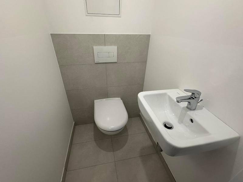 Kompaktes Gäste-WC mit modernen Fliesen, wandhängender Toilette und kleinem Waschbecken.