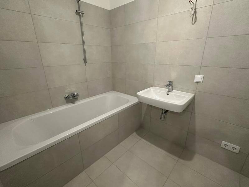 Modernes Badezimmer mit hellgrauen Fliesen, Badewanne und wandmontiertem Waschbecken.