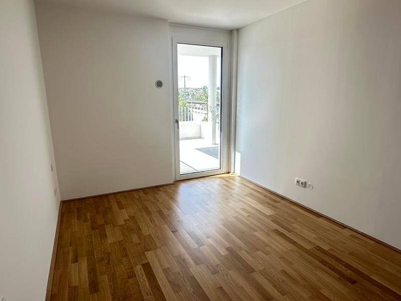 Helles, leeres Zimmer mit Holzboden und direktem Zugang zu einem Außenbereich.