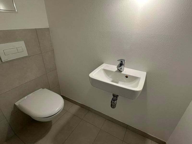 Gäste-WC mit Wand-WC und kleinem Waschbecken, teilweise gefliest.