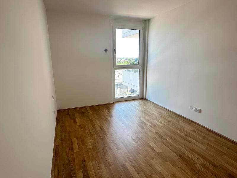 Leeres Schlafzimmer mit Parkettboden und einem Fenster, das viel Tageslicht hereinlässt.