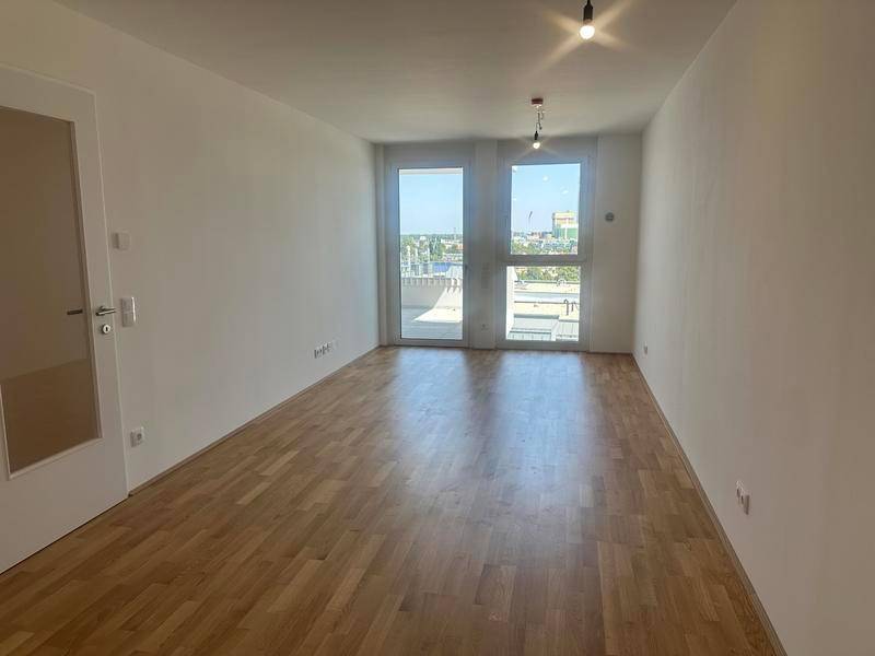 Helles, leeres Zimmer mit Parkettboden und großen Fenstern zum Außenbereich.