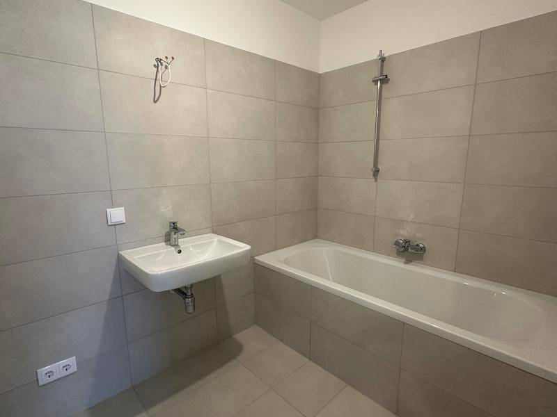 Modernes Badezimmer mit hellgrauen Fliesen, Waschbecken und Badewanne mit Duschfunktion.