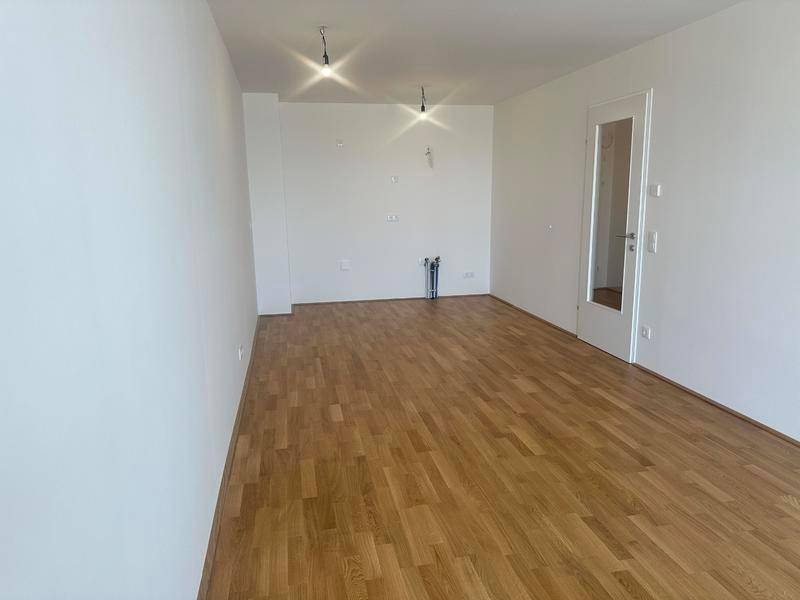 Leerer Raum mit Parkettboden und Anschlüssen für eine zukünftige Küche.