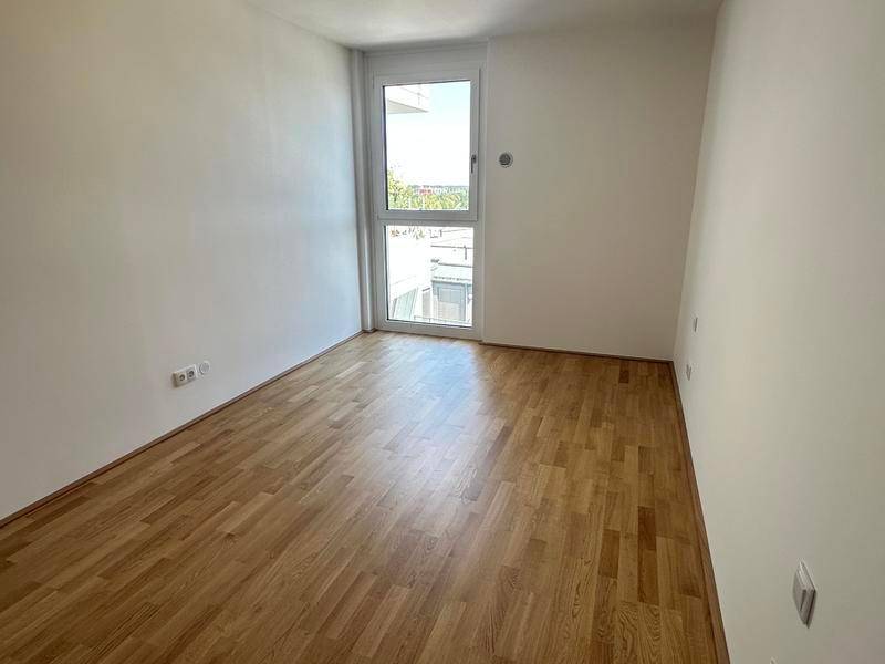 Freundliches Zimmer mit Parkettboden und großem Fenster, das viel Tageslicht hereinlässt.