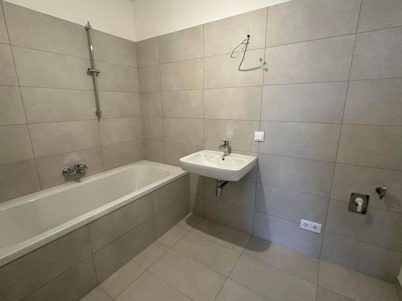 Modernes Badezimmer mit Badewanne, Waschbecken und hellen Fliesen, funktional und sauber.