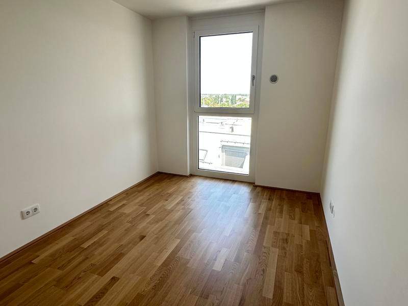 Helles Zimmer mit Parkettboden und einem großen Fenster, das viel Tageslicht hereinlässt.