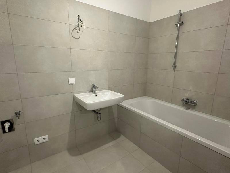 Modernes Badezimmer mit hellgrauen Fliesen, Badewanne und Waschbecken.