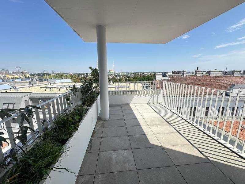 Langer Balkon mit Fliesenboden, Pflanzen und einem weiten Blick über die Dächer der Stadt.