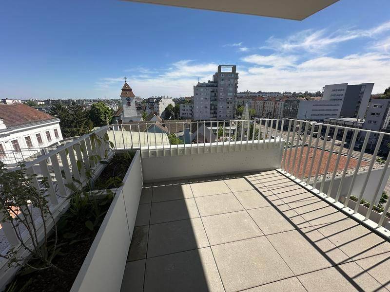 Geräumiger Balkon mit Fliesenboden, Pflanzenkübeln und weitem Blick über die Stadt.