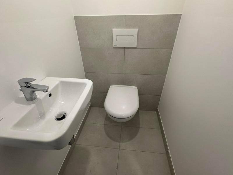 Separates Gäste-WC mit Wand-WC, kleinem Waschbecken und modernen Fliesen.