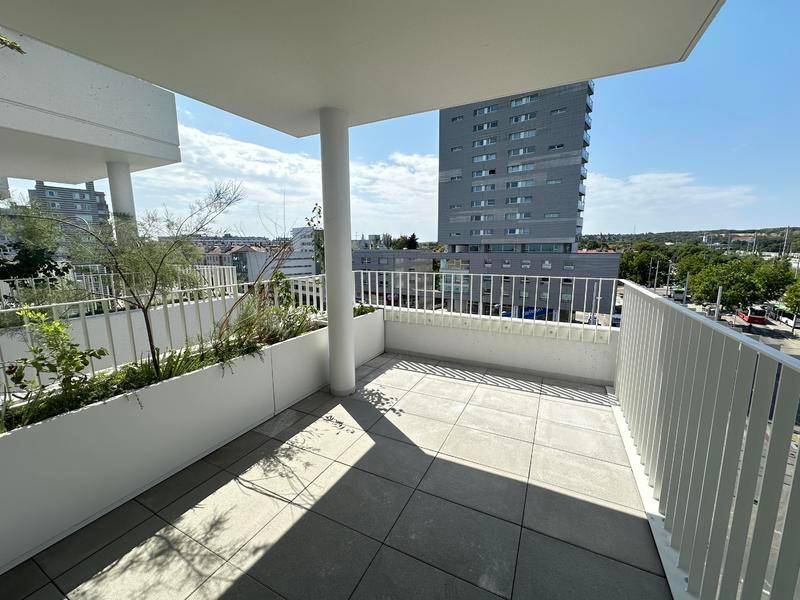 Geräumiger Balkon mit Fliesenboden und Blick auf die Stadt, umgeben von modernen Gebäuden.