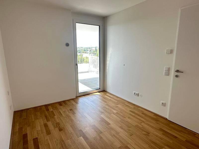 Helles Zimmer mit Holzboden und Zugang zu einem Balkon, ideal als Schlaf- oder Arbeitszimmer.