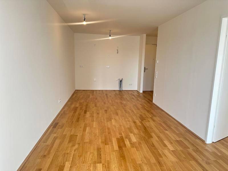 Leerer Raum mit Holzboden und Anschlüssen für eine Küche, bereit für die Installation.