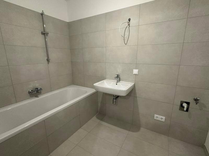 Modernes Badezimmer mit hellgrauen Fliesen, Badewanne und Waschbecken, in neuwertigem Zustand.