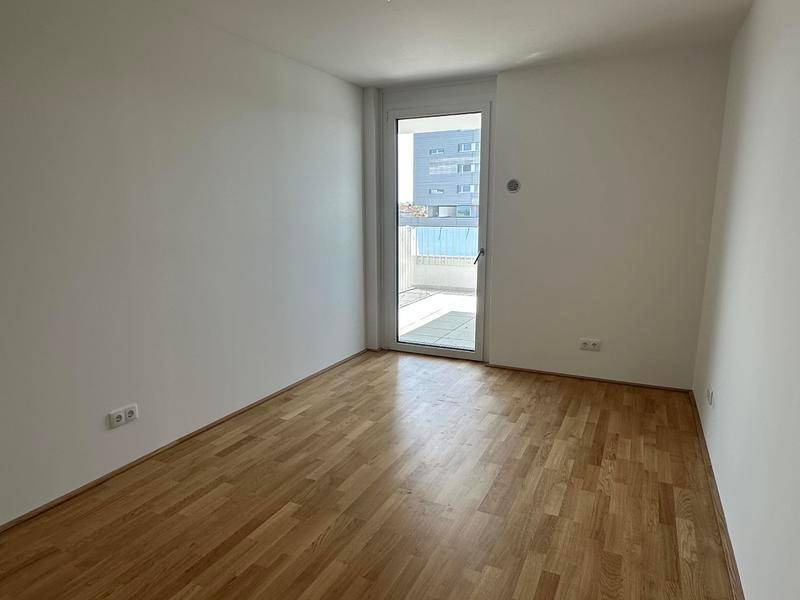 Helles Zimmer mit Parkettboden und Zugang zu einem Balkon, ideal als Schlaf- oder Arbeitszimmer.
