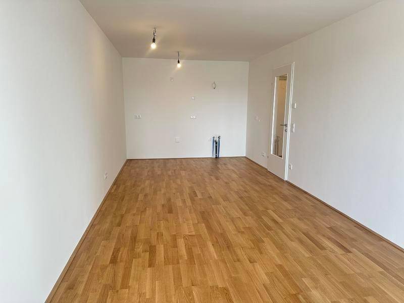 Leeres Zimmer mit hellem Parkettboden und Anschlussmöglichkeiten für eine Küche oder andere Geräte.