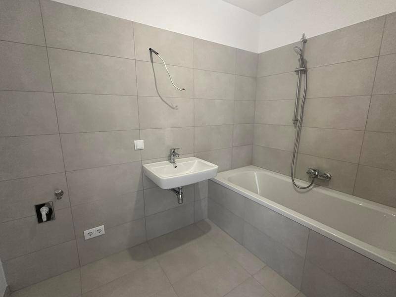 Modernes Badezimmer mit Badewanne, Waschbecken und hellgrauen Fliesen, bereit für die Endmontage.