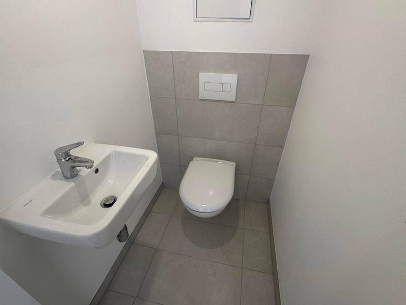 Helles Gäste-WC mit wandhängender Toilette und kleinem Waschbecken, modern gefliest.