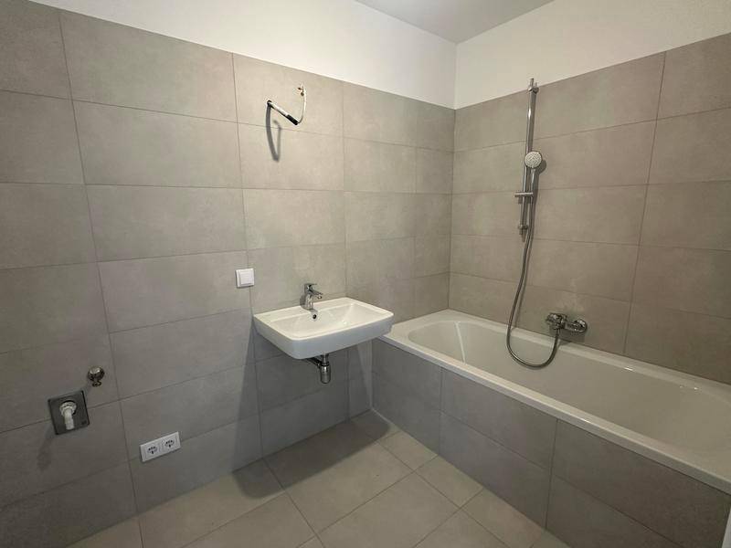 Modernes Badezimmer mit hellgrauen Fliesen, Badewanne und Waschbecken.
