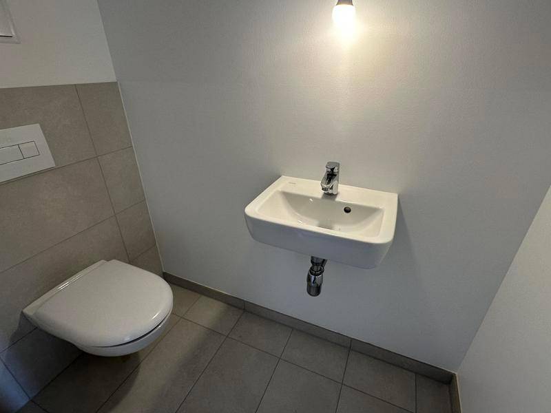 Separates Gäste-WC mit wandhängender Toilette und kleinem Waschbecken, modern gefliest und hell beleuchtet.