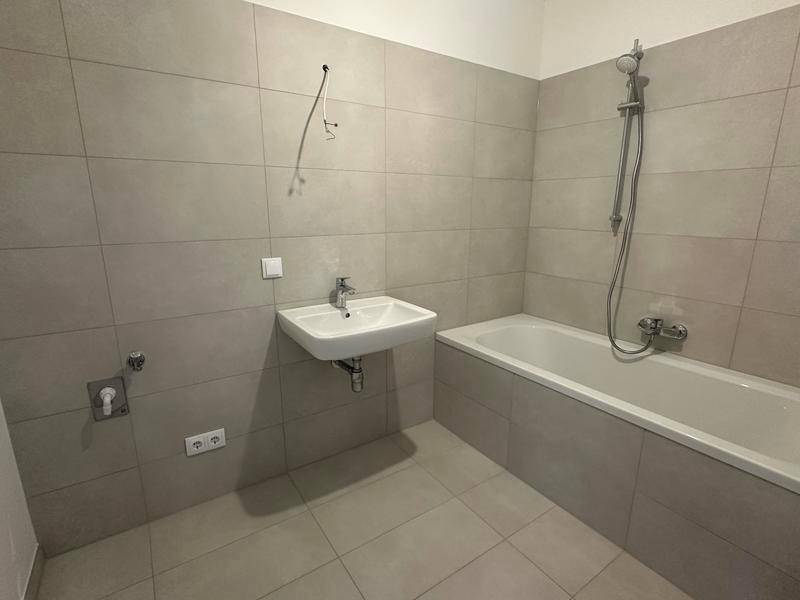 Modernes Badezimmer mit Badewanne, Duscharmatur und Waschbecken, komplett gefliest in neutralen Tönen.