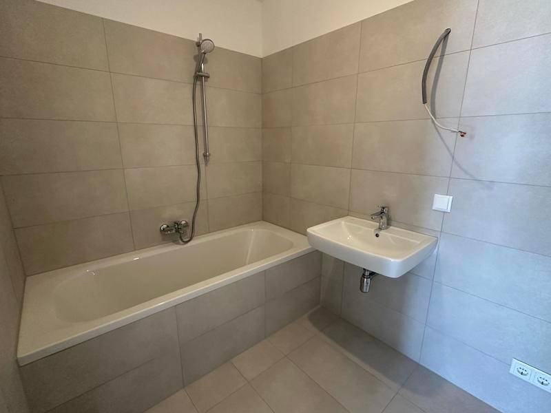 Modernes Badezimmer mit Badewanne, Duscharmatur und einem einzelnen Waschbecken, gefliest in hellen Farbtönen.