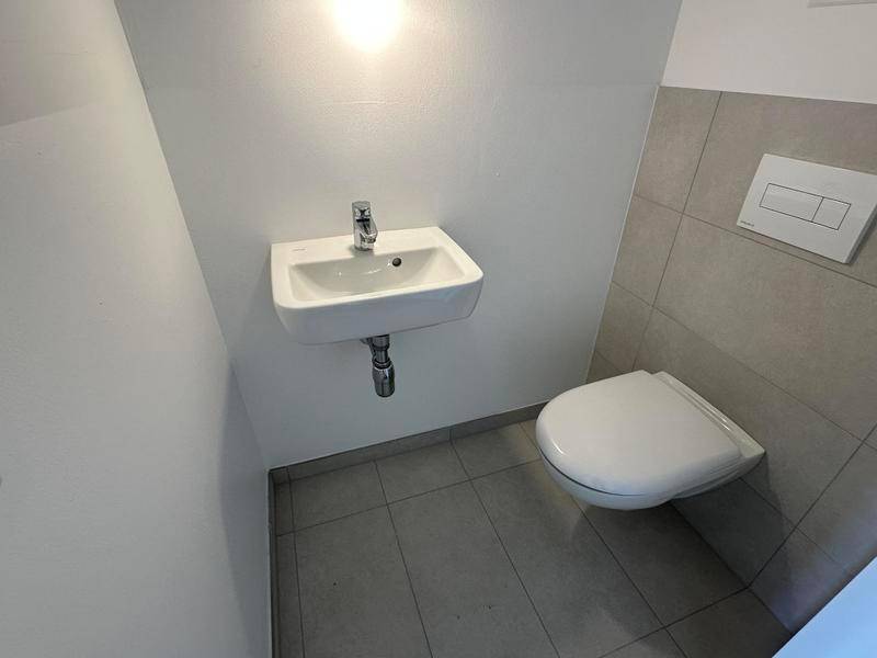 Kleines Gäste-WC mit wandhängender Toilette und einem kompakten Waschbecken, teilweise gefliest.