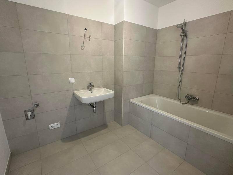 Modernes Badezimmer mit Badewanne, Duscharmatur und Einzelwaschbecken, hell gefliest.