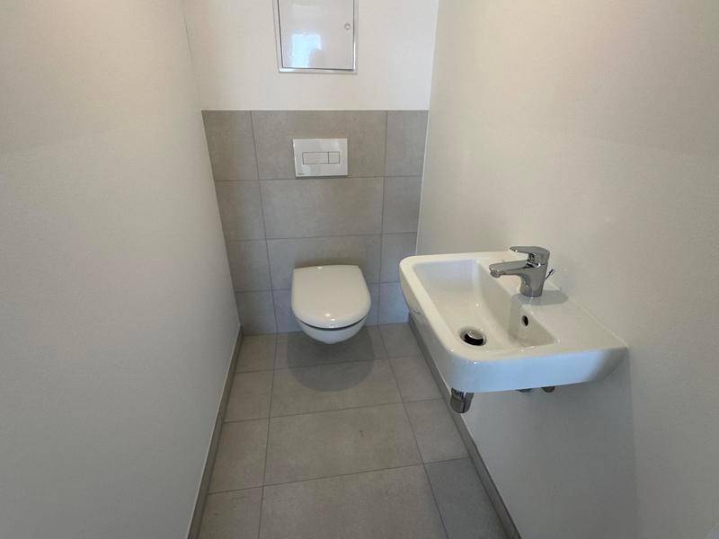 Kleines Gäste-WC mit wandhängender Toilette und kompaktem Waschbecken, teilweise gefliest.