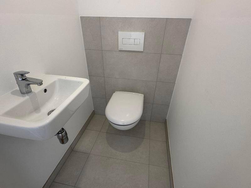 Separates Gäste-WC mit wandhängender Toilette und kleinem Waschbecken in minimalistischem Design.