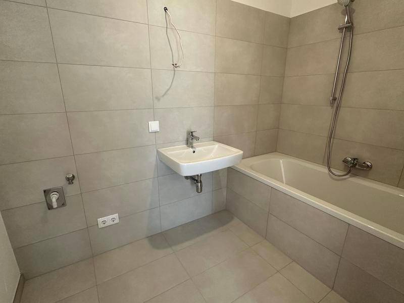Modernes Badezimmer mit Badewanne, Waschbecken und hellgrauen Fliesen in neuwertigem Zustand.