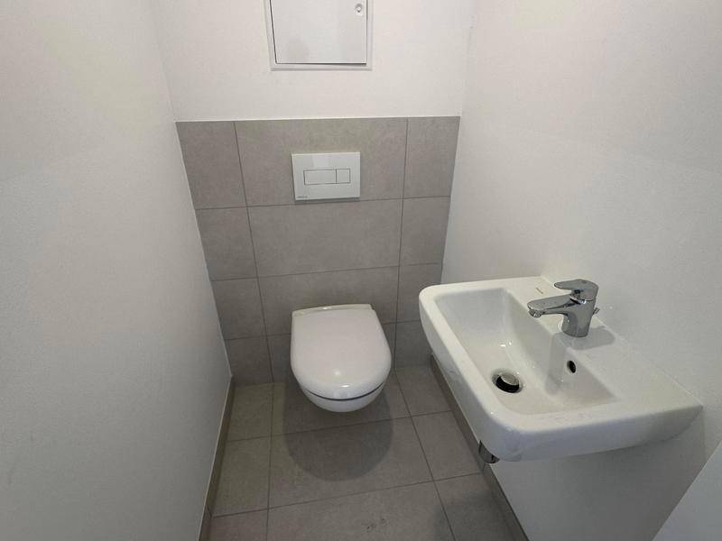 Kleines Gäste-WC mit wandhängender Toilette und kompaktem Waschbecken, teilweise gefliest in neutralen Farben.