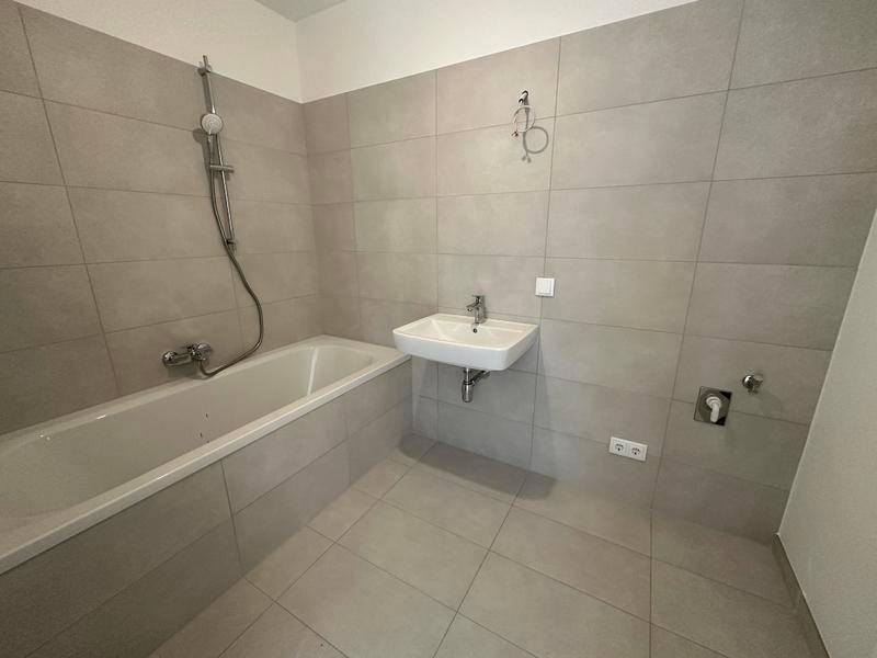 Modernes Badezimmer mit Badewanne, Duscharmatur und Waschbecken, gefliest in hellgrauen Tönen.