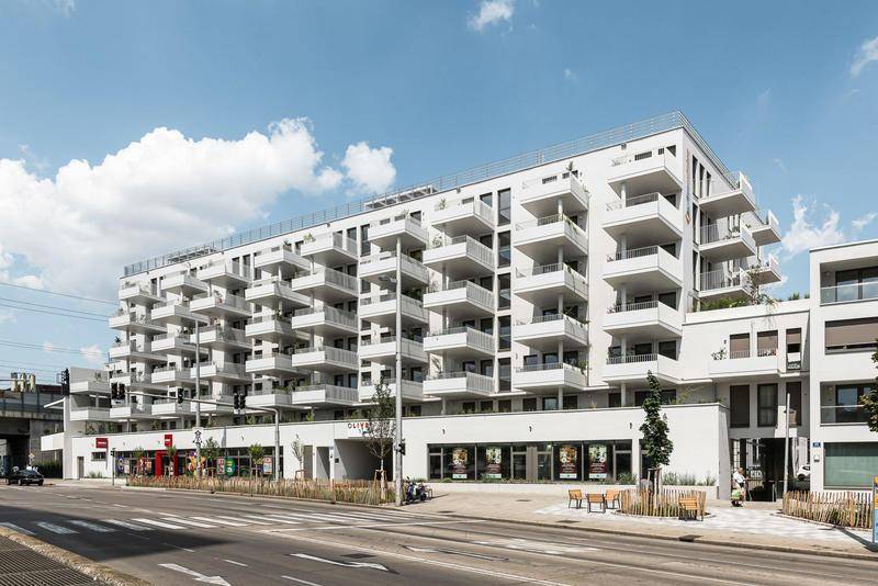 Moderne Wohnanlage mit zahlreichen Balkonen und Geschäften im Erdgeschoss, an einer belebten Straße gelegen.