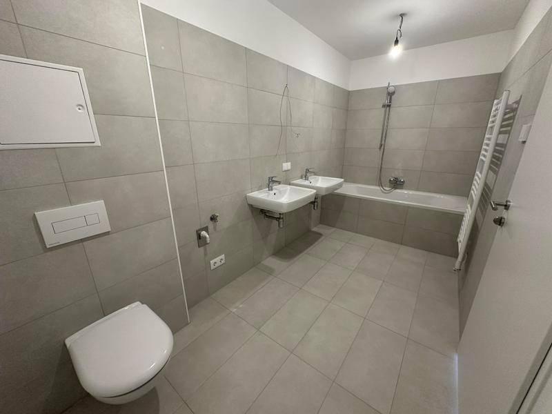 Modernes Badezimmer mit grauen Fliesen, zwei Waschbecken, Badewanne und beheiztem Handtuchhalter.
