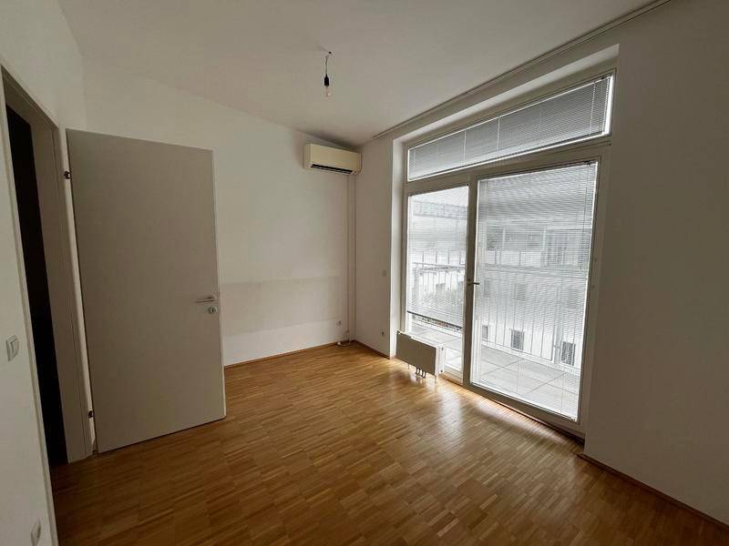 Leeres Schlafzimmer mit Parkettboden, Klimaanlage und großem Fenster mit Blick nach draußen.