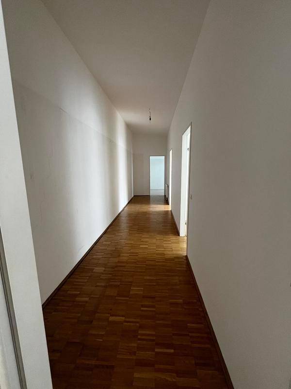 Langer, heller Flur mit Parkettboden und weißen Wänden, der zu weiteren Räumen führt.