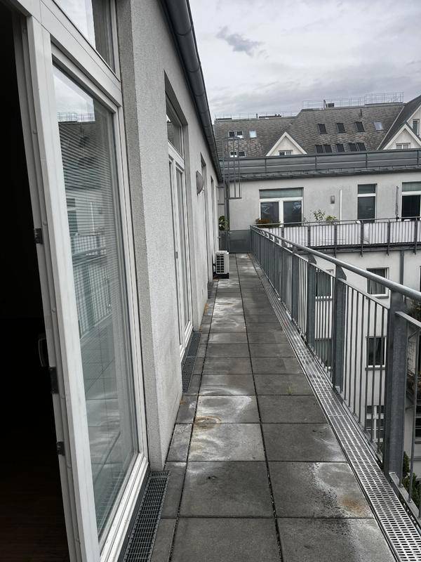 Schmaler Außenbalkon mit Fliesenboden und Metallgeländer, der entlang der Fassade verläuft.