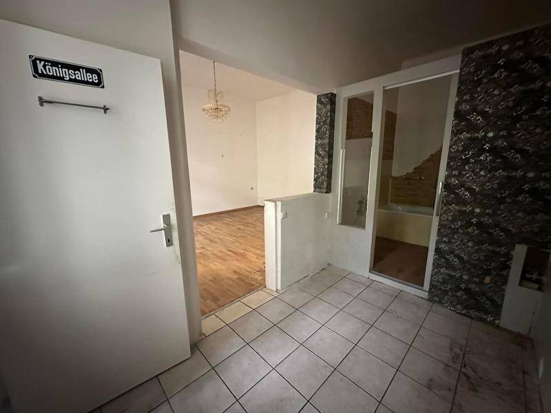 Eingangsbereich mit Fliesenboden und Blick in ein angrenzendes Zimmer mit Holzboden.