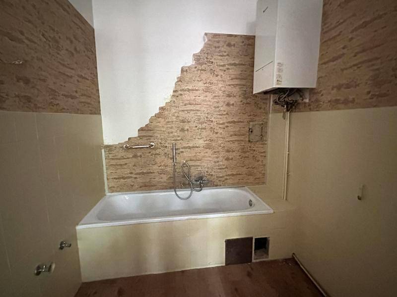 Badezimmer mit Badewanne, Wandfliesen und sichtbarem Warmwasserbereiter, renovierungsbedürftig.
