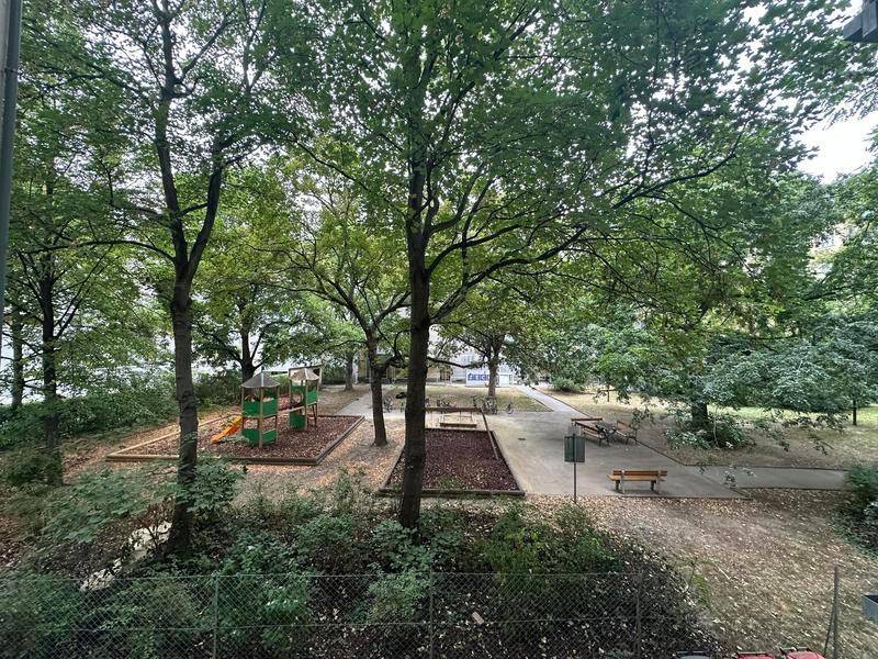 Grüner Außenbereich mit Kinderspielplatz und vielen Bäumen, ideal für Familien.