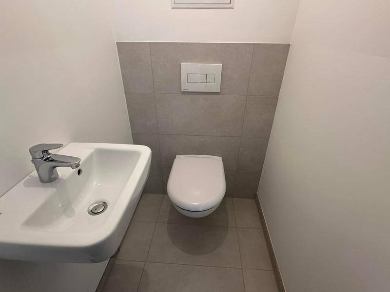 Gäste-WC mit wandhängender Toilette und kleinem Waschbecken in neutralen Farben.