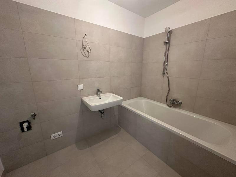 Modernes Badezimmer mit Badewanne, Waschbecken und hellgrauen Fliesen.