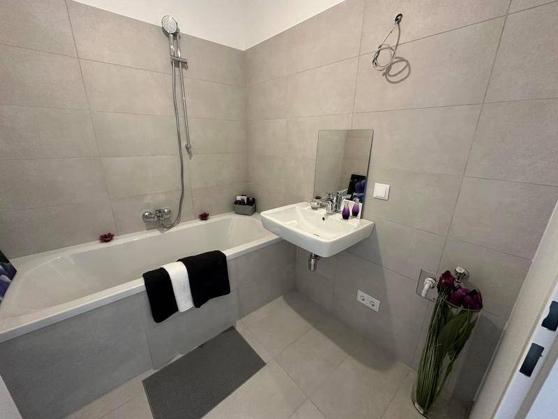 Modernes Badezimmer mit Badewanne, Waschbecken und grauen Fliesen.