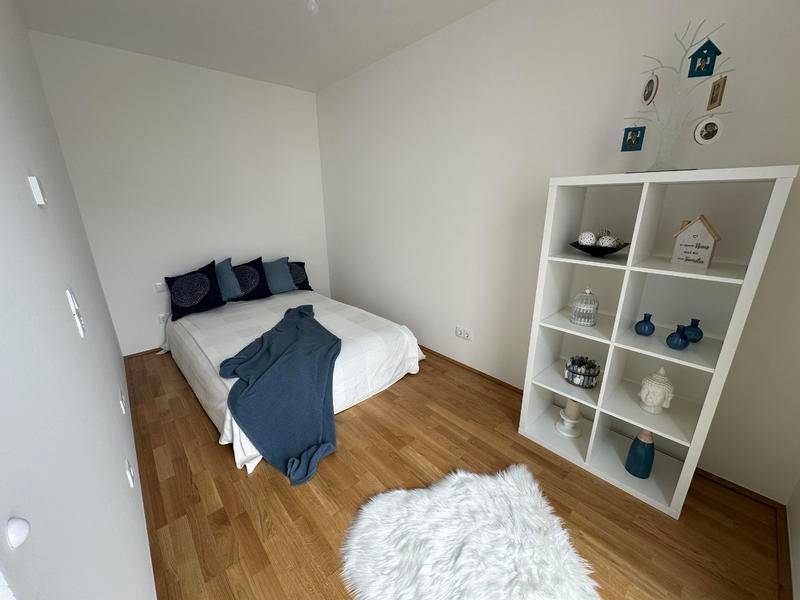Modern eingerichtetes Schlafzimmer mit Holzboden und weißem Regal.